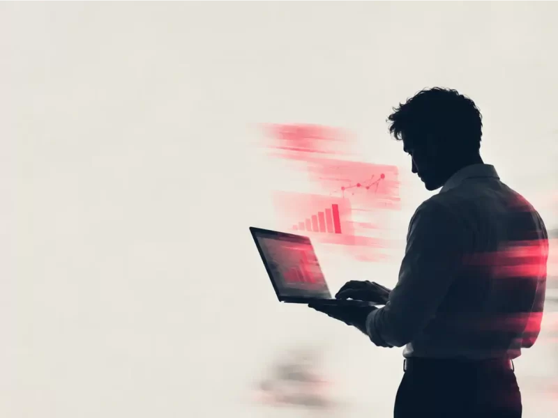 Uomo in controluce che consulta un portatile con grafici di crescita in rosso, per rappresentare il budget delle campagne Meta Ads